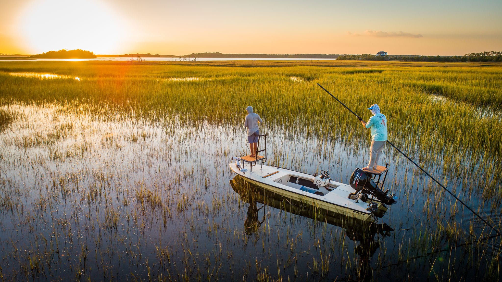 Two anglers fly fishing from a boat in a Lowcountry marsh at sunset