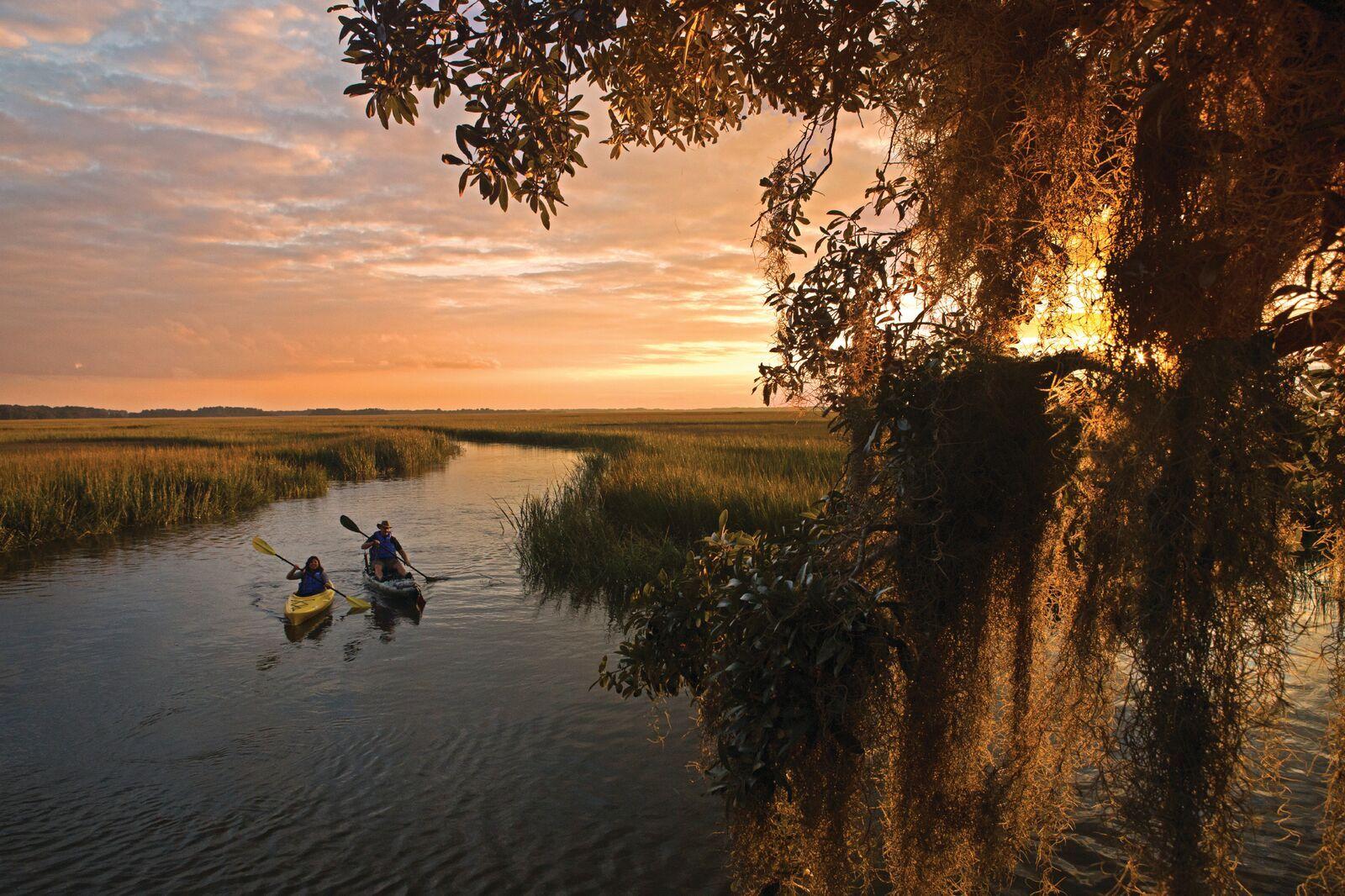 Two kayakers paddling through a Lowcountry marsh at sunset