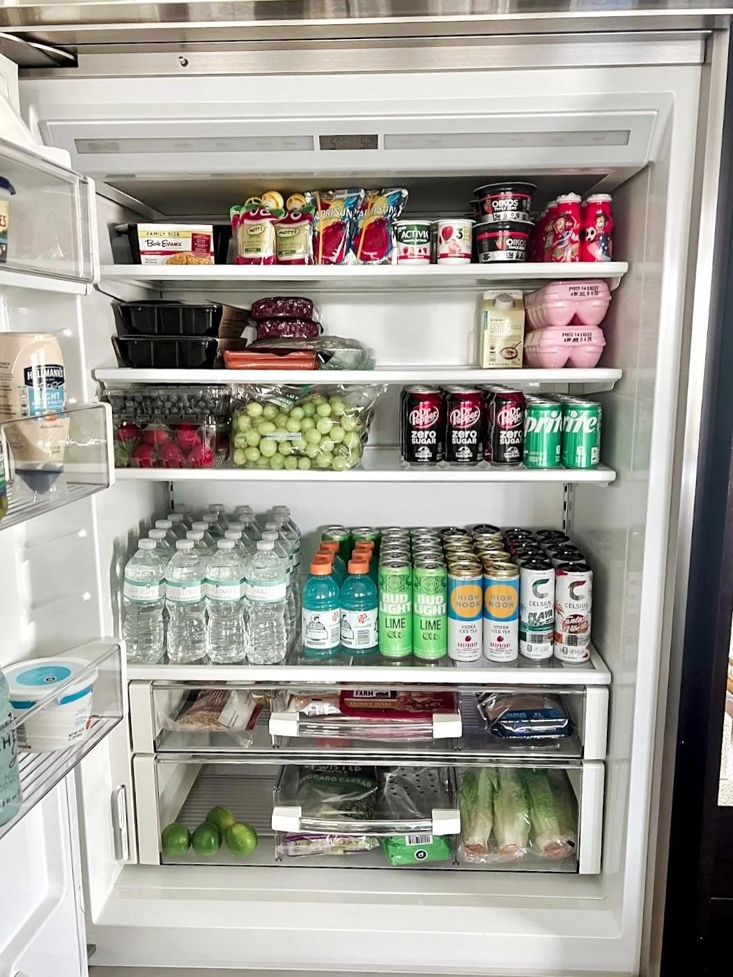 An open refrigerator fully stocked and faced with groceries, ready for arriving guests